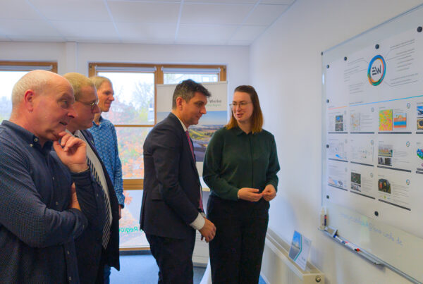 Geschäftsführerin Stefanie Kleine steht mit Landrat Henry Graichen und den Bürgermeistern Uwe Weigelt und Bernd Laqua vor einem Whiteboard mit einem Aushang zum Projekt Energiewerkstatt Wurzener Land.